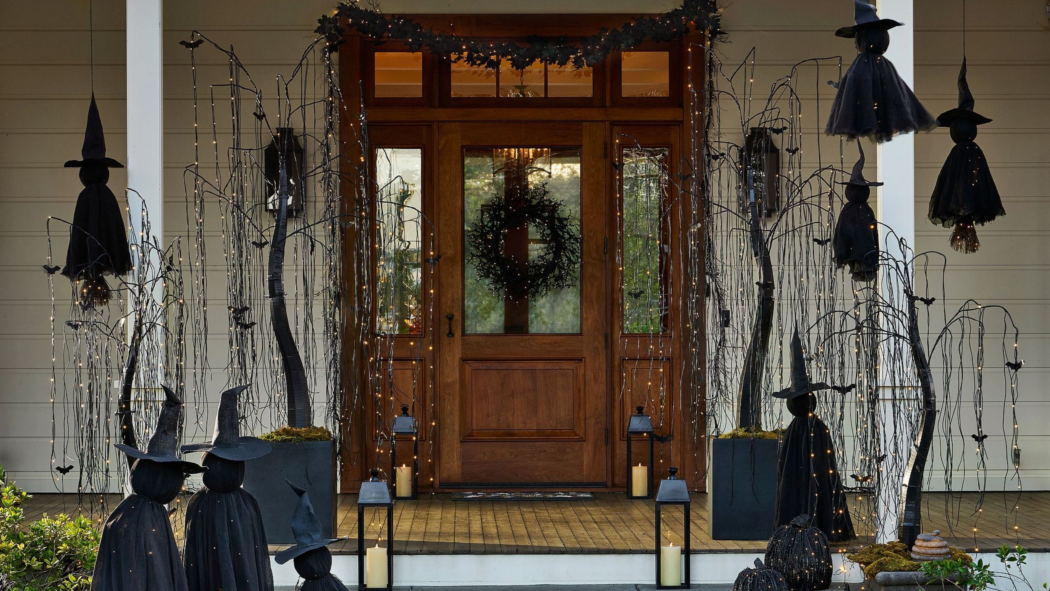 Front porch area decorated with gothic Halloween lights, including twinkling willow trees, witches, lanterns, and an all-black wreath.