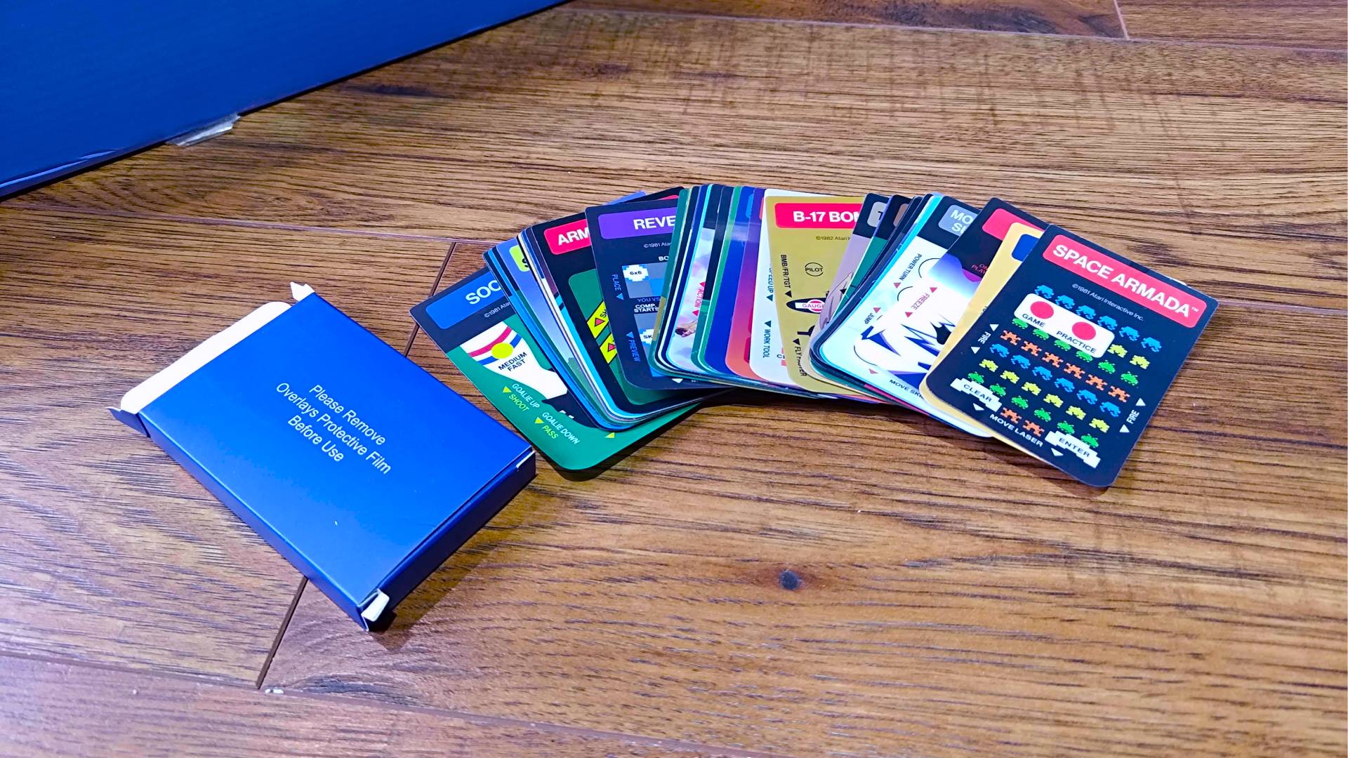 Intellivision Sprint overlays spread out next to box on woodgrain floor.