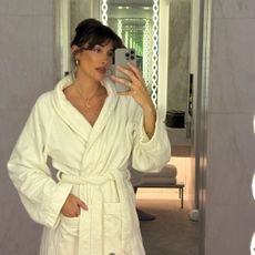A woman taking a mirror selfie in the bathroom wearing a white robe