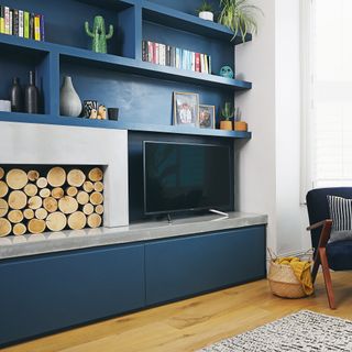 navy blue wall in living room with built in shelves, tv and stacked fire wood