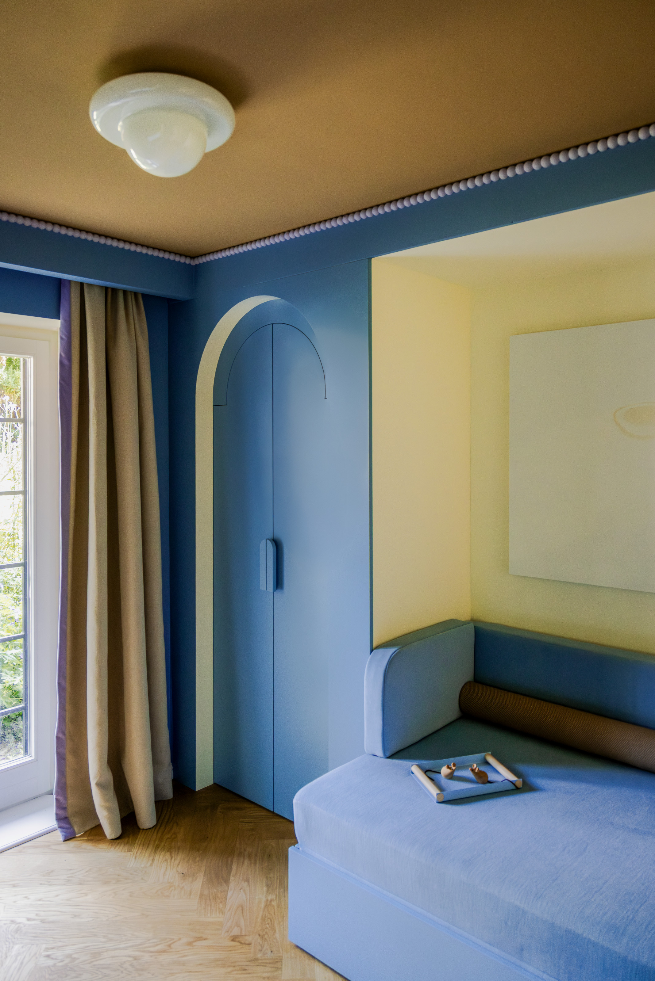 Bedroom with yellow and blue walls, built-in wardrobe with curved door, blue built-in daybed and globe ceiling light