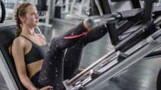 A woman sits on a leg press machine with her legs extended.