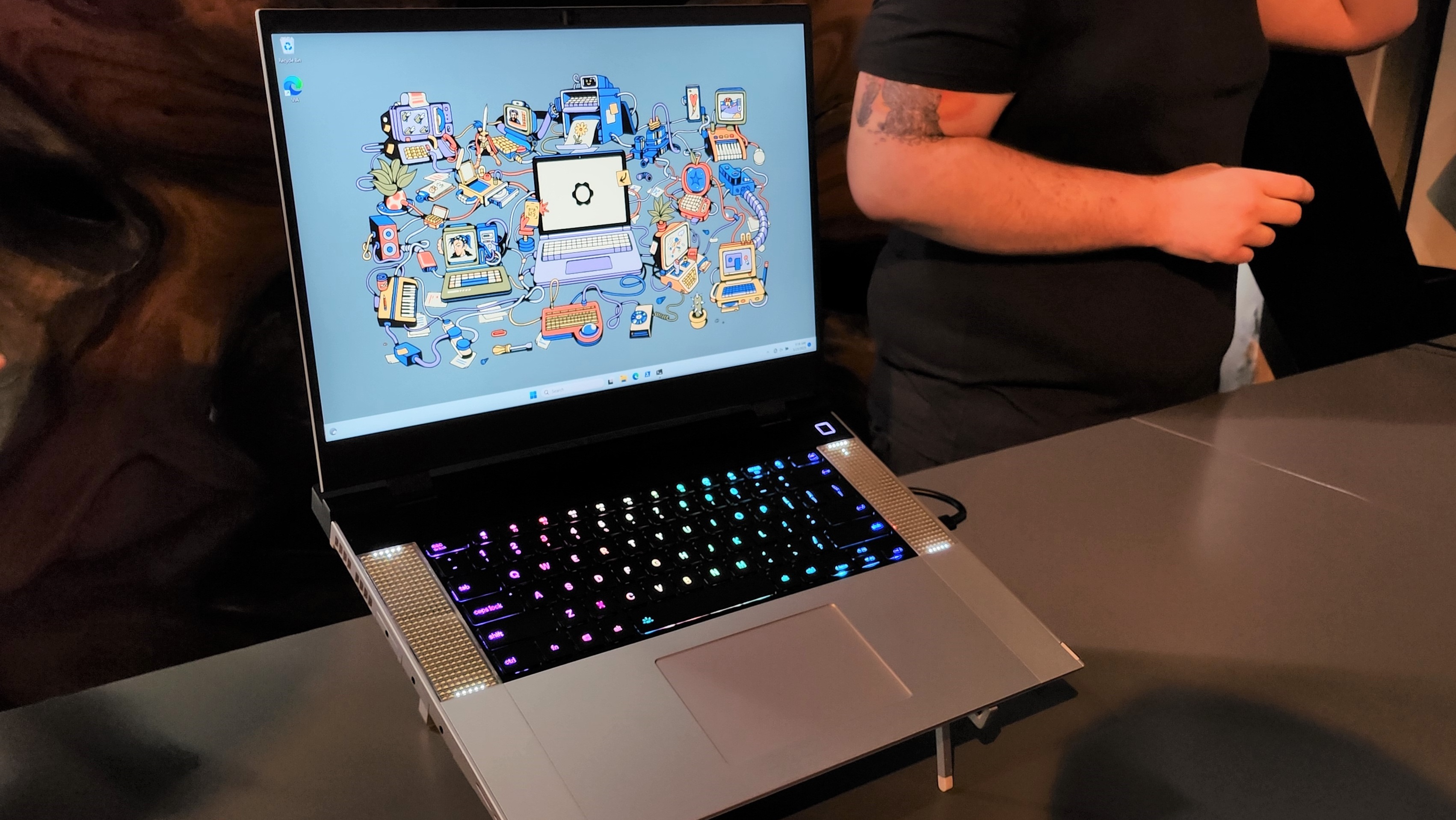 head on image of open Framework gaming laptop on presentation floor, abstract desktop background in Windows with RGB keyboard, speakers on side, chrome furnishing and slim black bezels