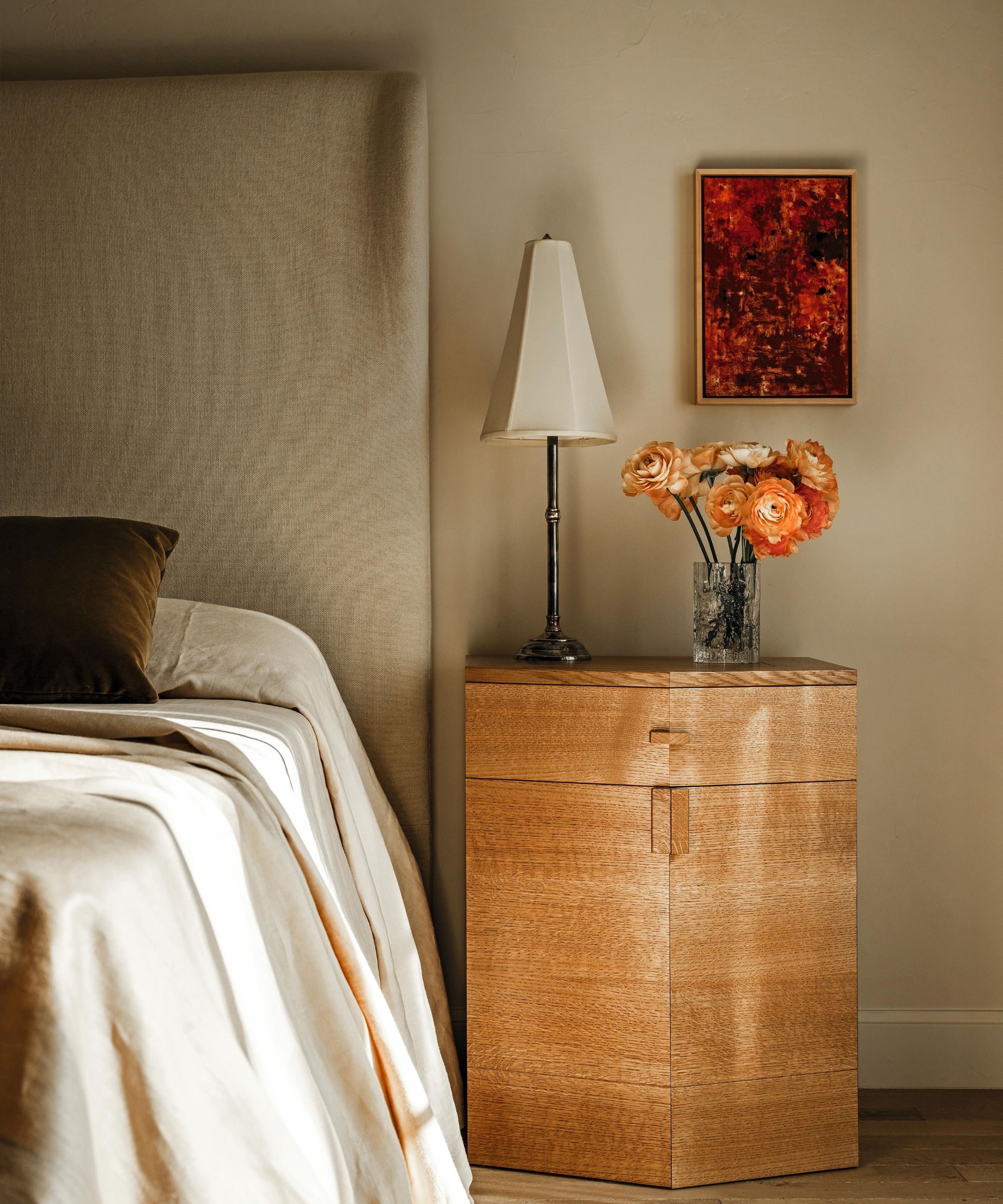 a beige layered bedroom with linen headboard and art decor style wooden nightstand