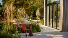 modern patio garden with planting island featuring ornamental grasses, outdoor furniture and paving slabs