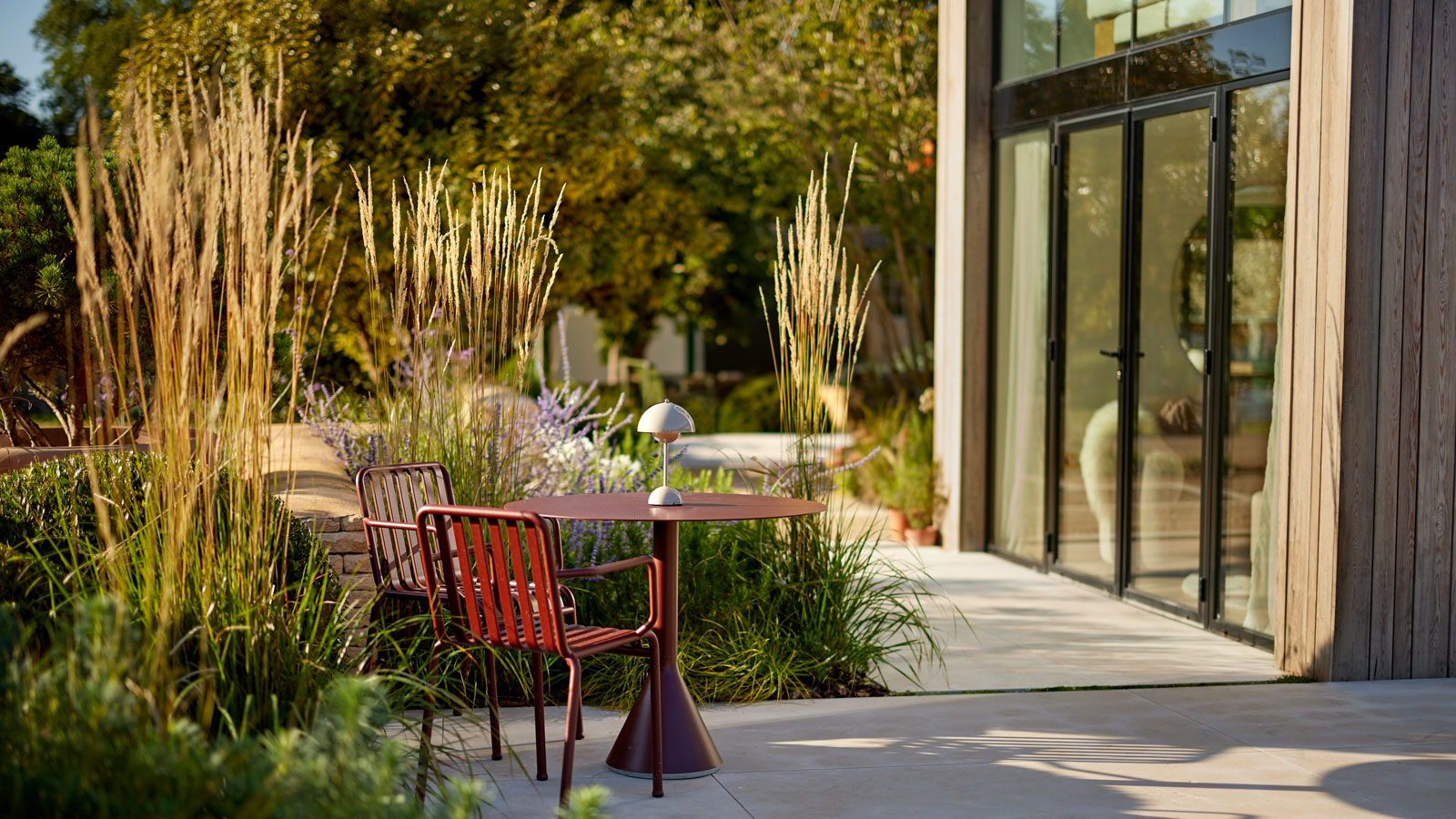 modern patio garden with planting island featuring ornamental grasses, outdoor furniture and paving slabs