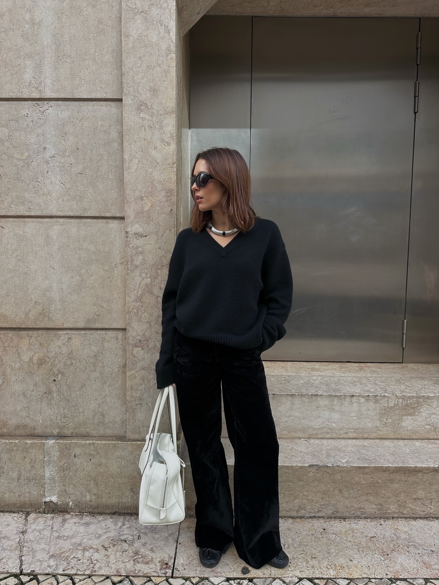 An image of @deborabrosa wearing a black V-neck jumper and black wide-leg trousers.
