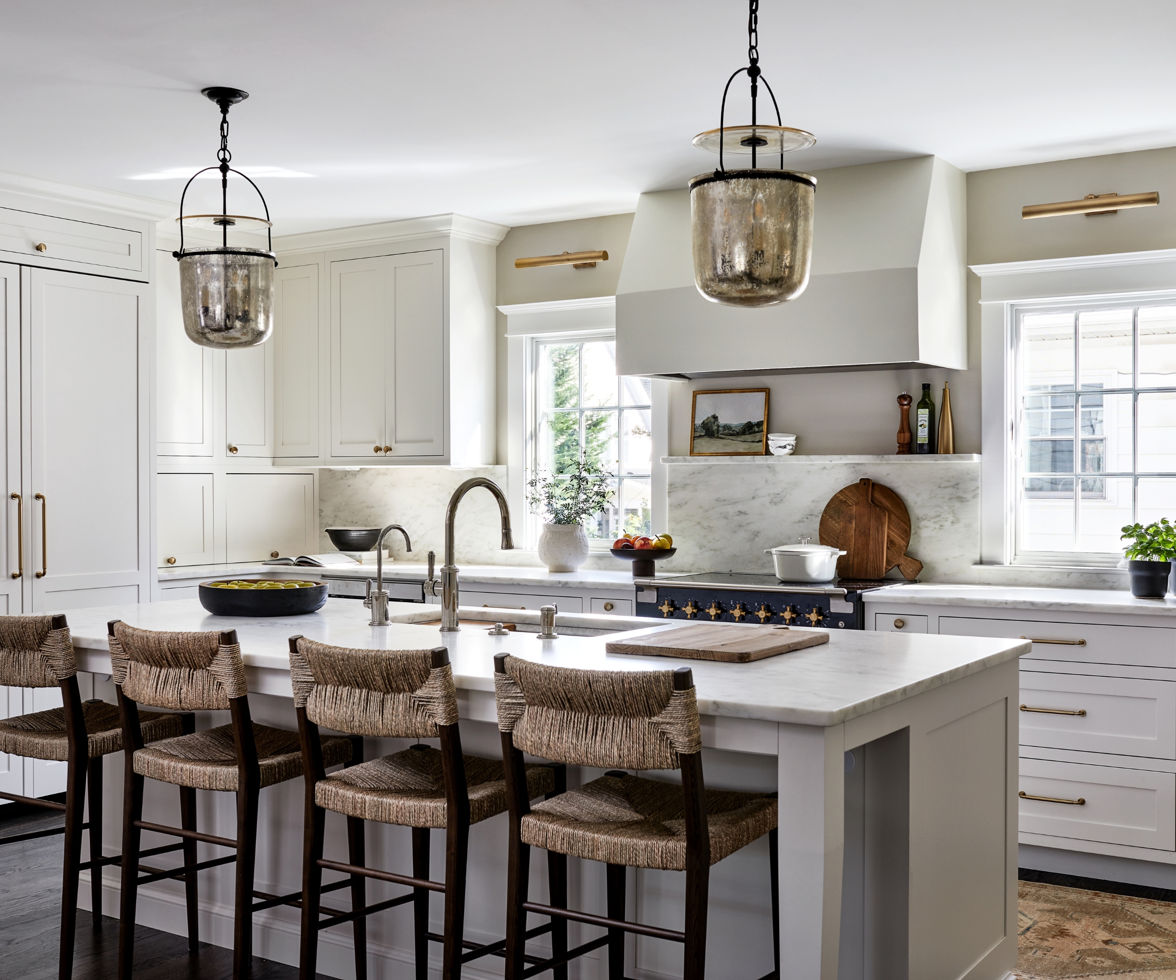 A white kitchen with two island pendant light, two brass wall sconces above the windows, and a shelf decorated with fall decor
