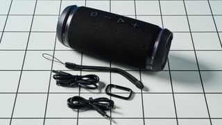 a black portable bluetooth speaker with LED panels sits atop a white table with a blue background