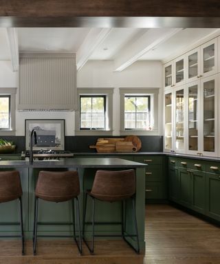 forest green kitchen with black quartz countertops, hardwood floor, leather bar stools, glazed counter units, black faucet, island with sink