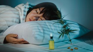 Young woman asleep in bed with CBD oil and capsules beside her