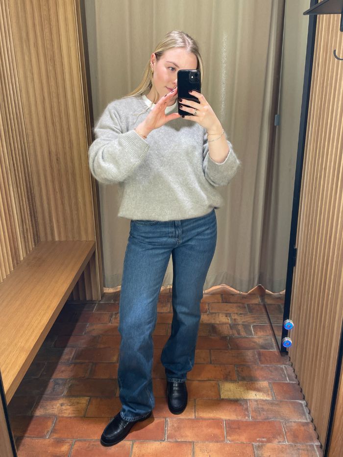 Woman wears grey jumper, blue jeans and black loafers