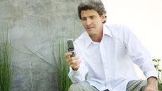 An older man looks at his flip phone while sitting outside.