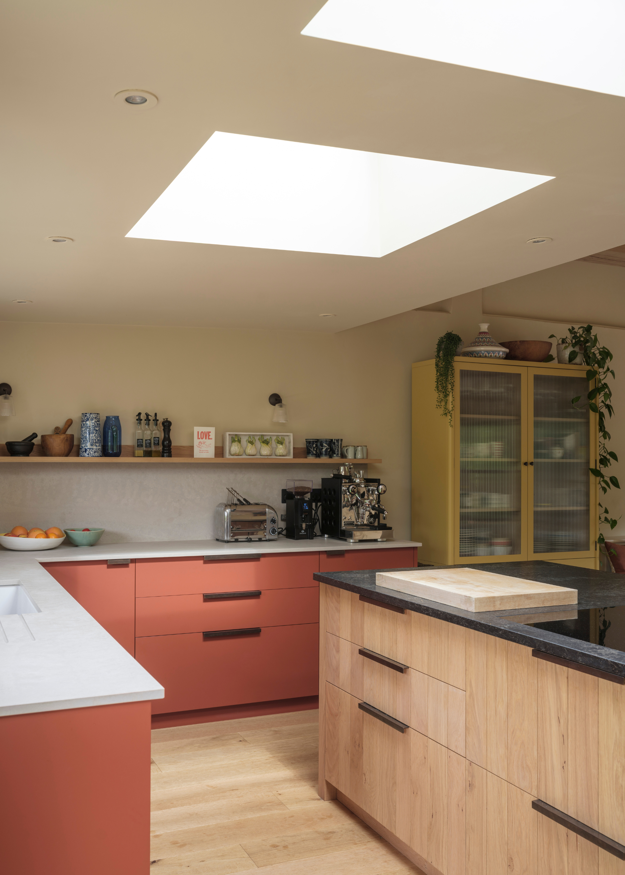 light wooden island counter with peach painted cabinetry surrounding in a light-filled kitchen