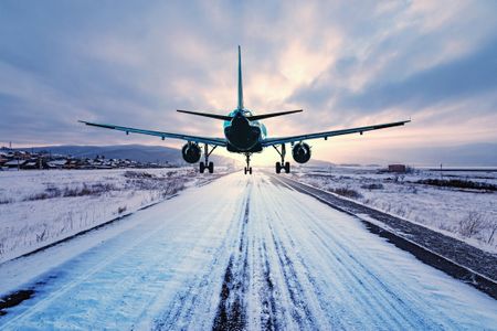 A passenger plane landing on a snowy highway at winter evening time.