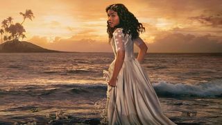 Mia Isaac – star of Black Cake season 1 on Hulu – gathers her elegant dress in her hands and looks over her shoulder on at sunset on a tropical beach.