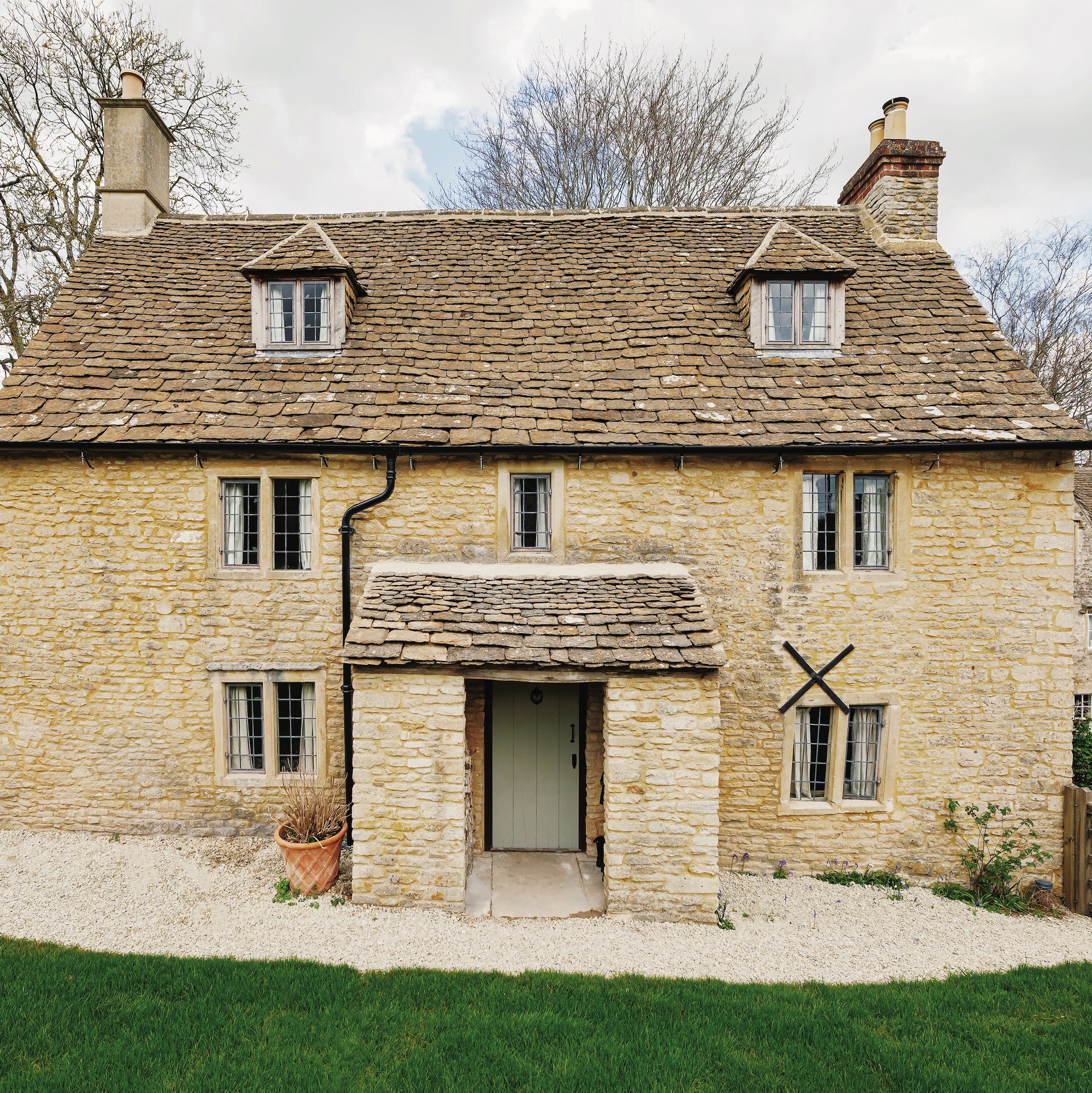 exterior of double fronted cotswold cottage with stone porch and dormer windows in roof