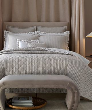 Gray comforter set on a beige headboard with a beige chaise lounge against a beige curtain.