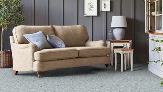 Living room with grey wall paneling a beige upholstered sofa and sage green patterned carpet
