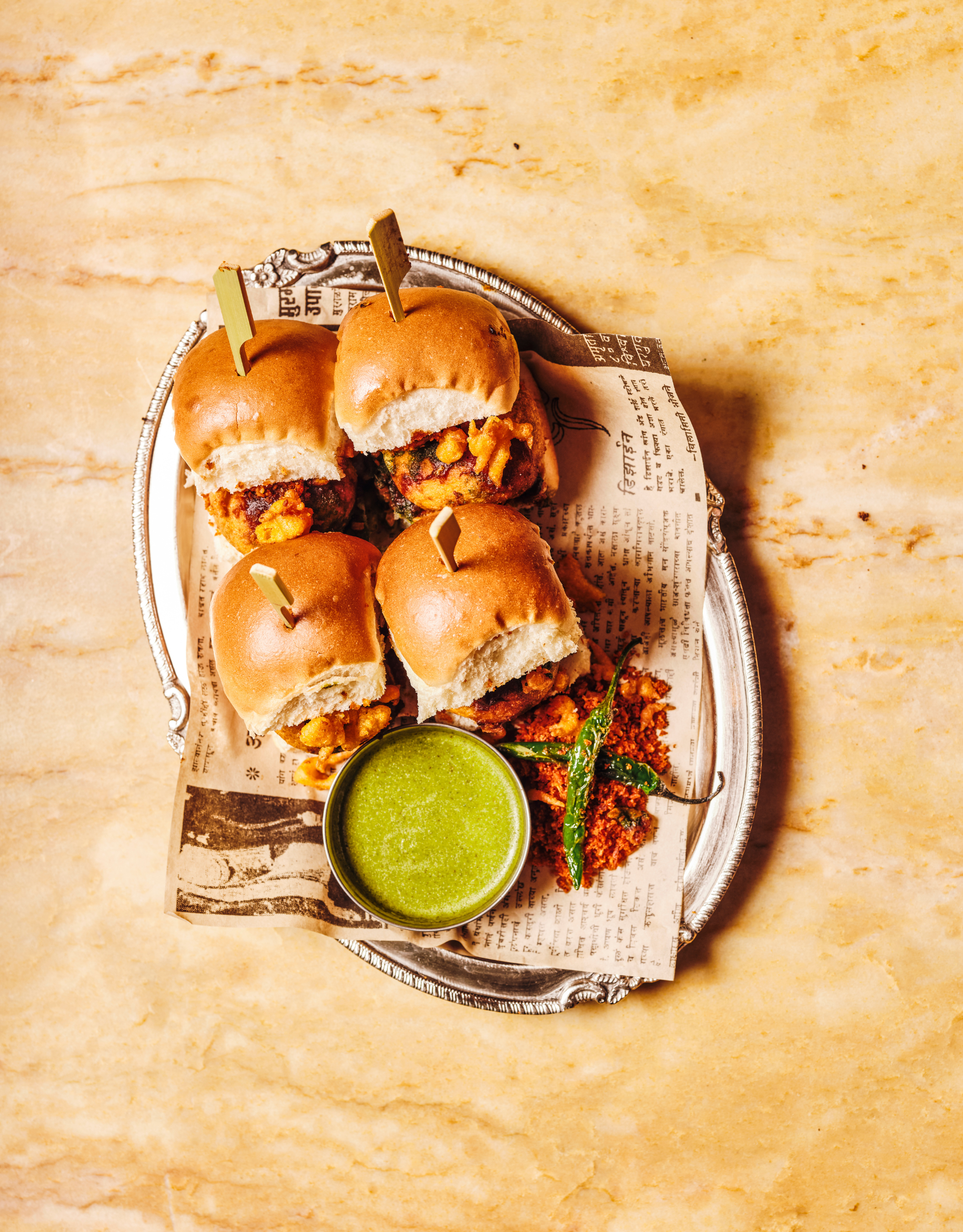 A silver plate with an ornate border serving up vada pav from Dishoom