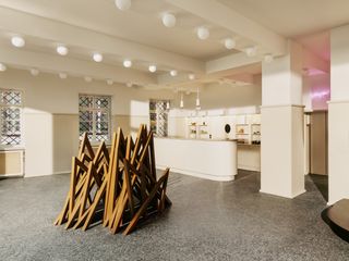Bright area, with white and beige walls, a bar to the far wall with shelves behind it. A wooden structure is in the center, made out of boards that are connected in the shape of a triangle.
