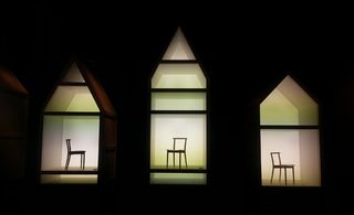 Black background, three lit up display units with triangle shape top, each has a chair in the centre