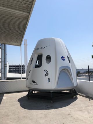 A model of SpaceX’s Crew Dragon spacecraft, as seen during a media day at the company’s headquarters in Hawthorne, California, on Aug. 13, 2018. In the background is the first SpaceX Falcon 9 rocket first stage ever to successfully land during an orbital mission.