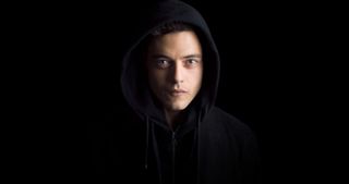 Rami Malek wearing a dark hoodie against a black background in Mr. Robot