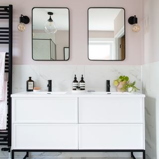 A pink bathroom with a double sink framed by a wall sconce on either side