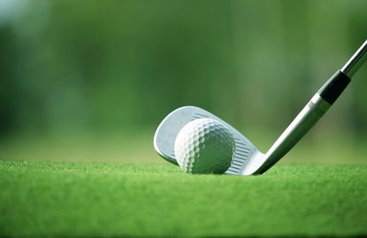 A golf iron addressing a golf ball on a green mat