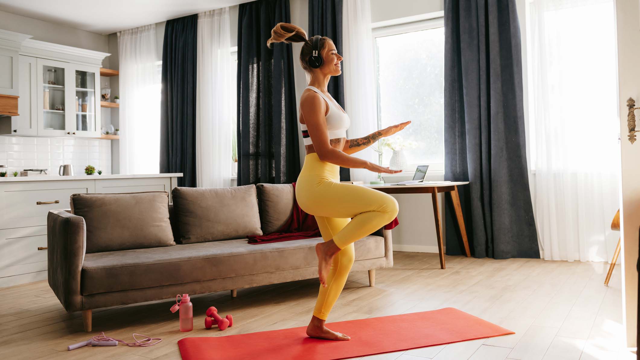 Woman in yellow leggings wearing headphones doing a workout at home on a red yoga mat