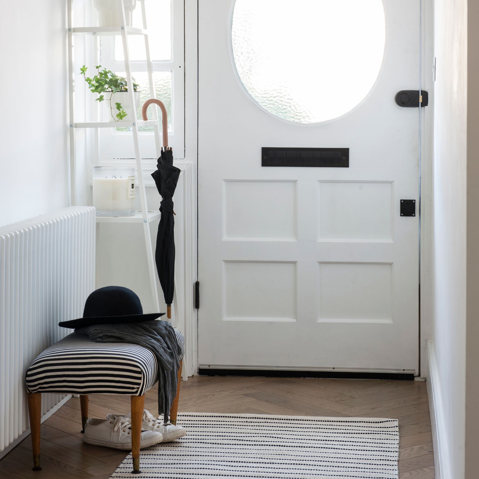White painted hallway with a white wooden front door, umbrella stand and a stool with a hat on it