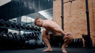 Athletic male in shorts at the gym performing a low squat hold while stretching out his hips