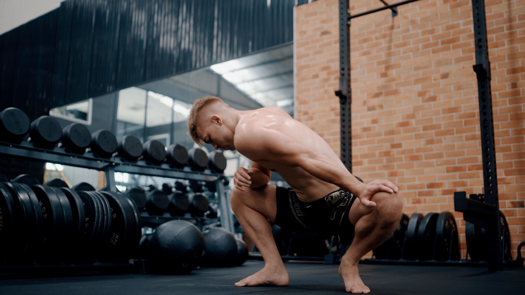 Athletic male in shorts at the gym performing a low squat hold while stretching out his hips