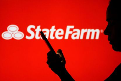 State Farm logo is seen in the background of a silhouetted woman holding a mobile phone