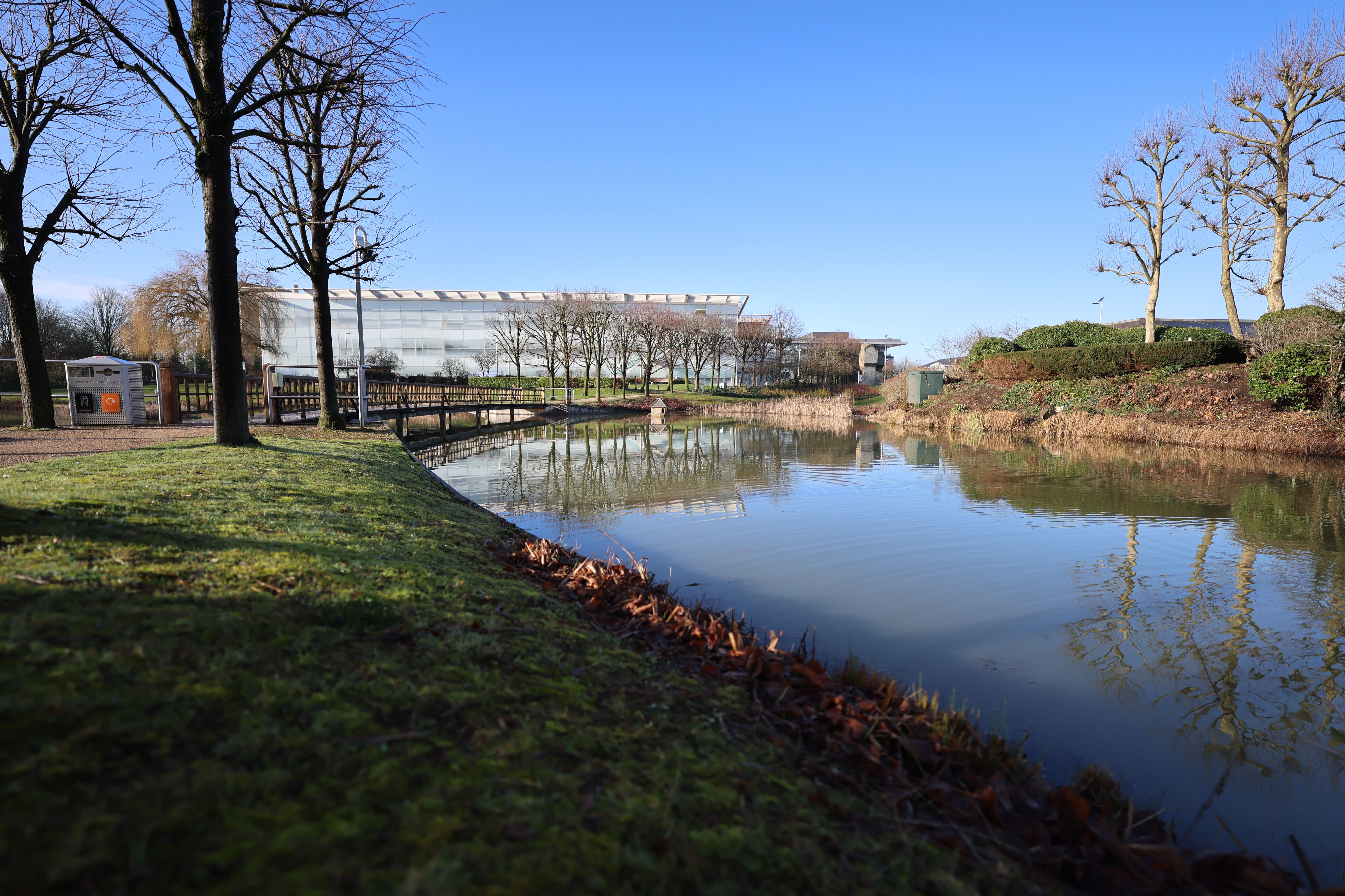  a bridge crossing a lake below a blue sky with office buildings in the background