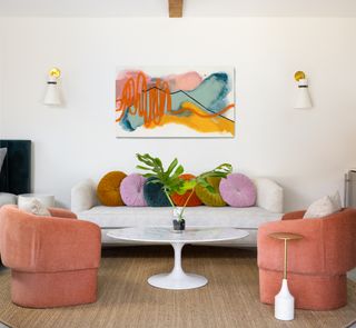 Small living room with white sofa, coral armchairs and abstract artwork
