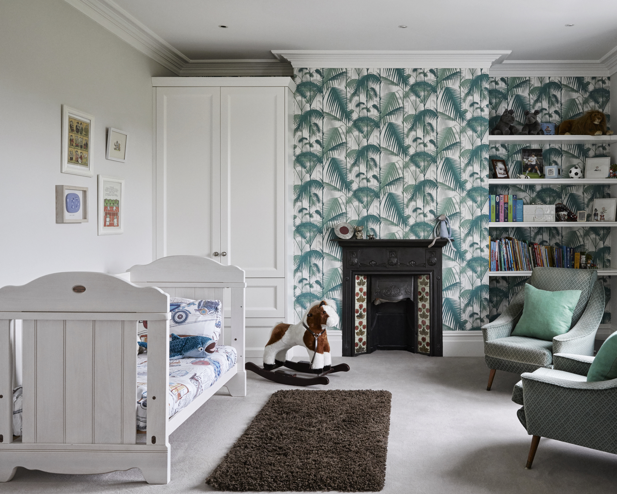 A baby boy nursery idea with green and white palm tree wallpaper, green armchairs and white crib.