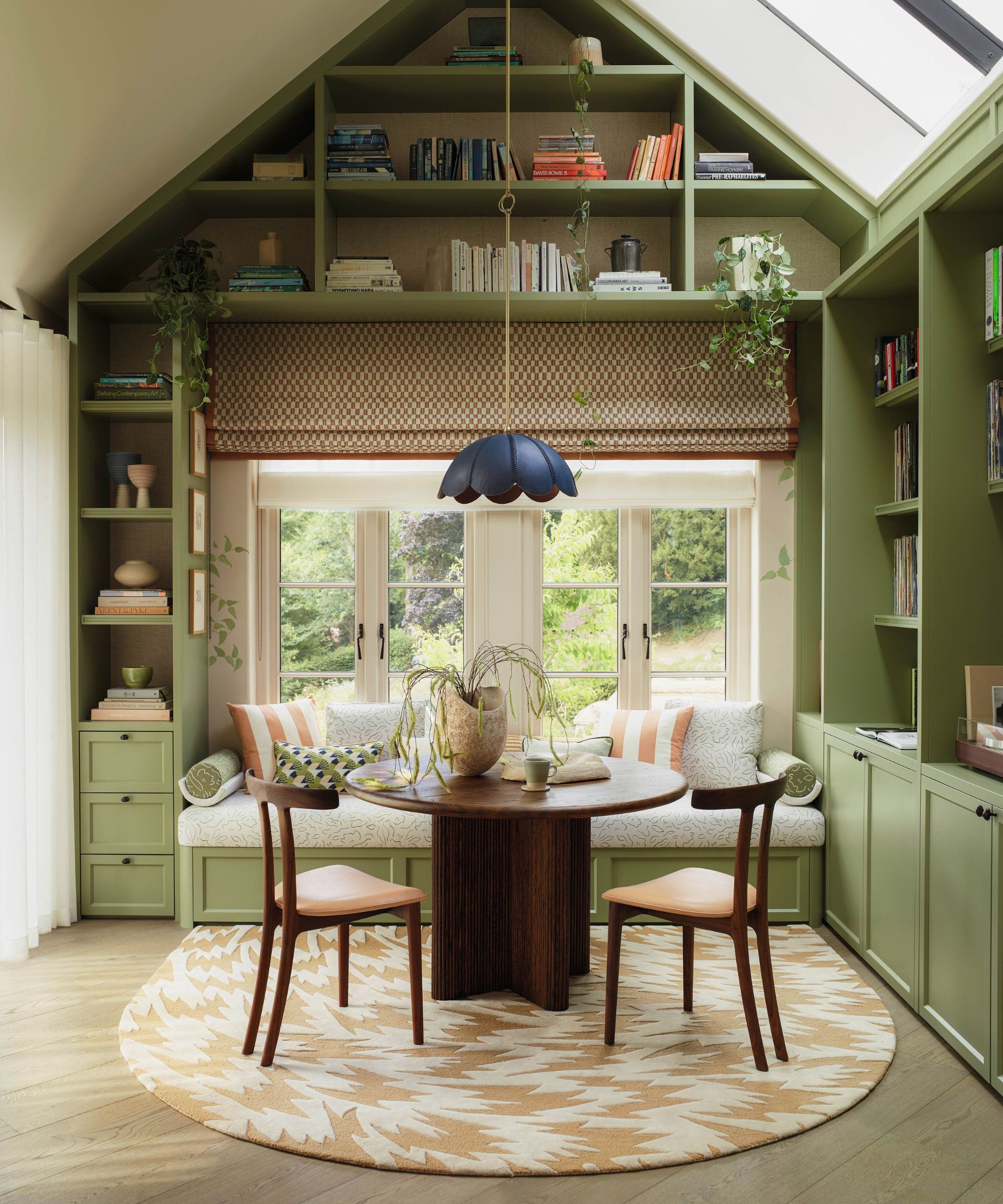 a sunroom with a vaulted ceiling, green bespoke joinery, a round table and chairs