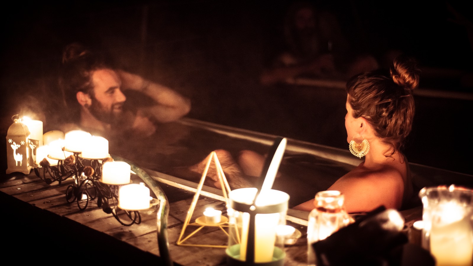 A couple glows in romantic candle light in outdoor bath in nature