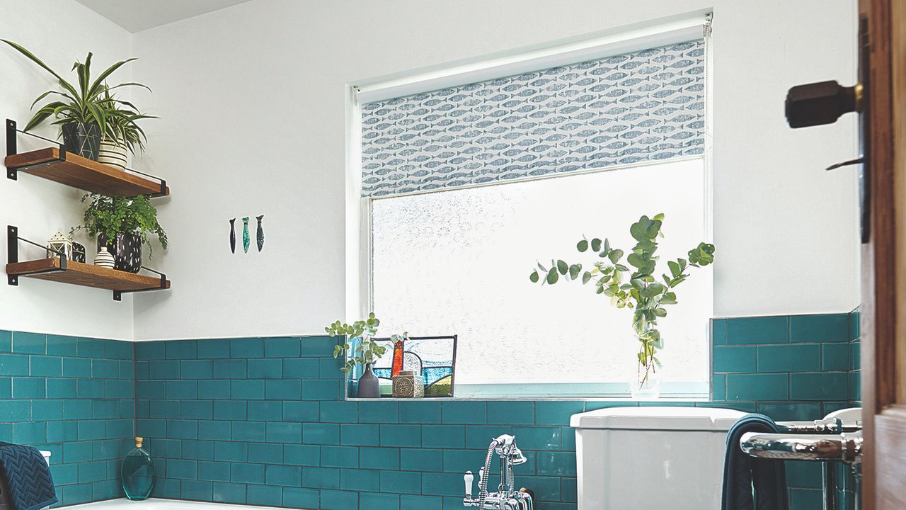 A bathroom with turquoise tiles and fish-print roller blinds in the window