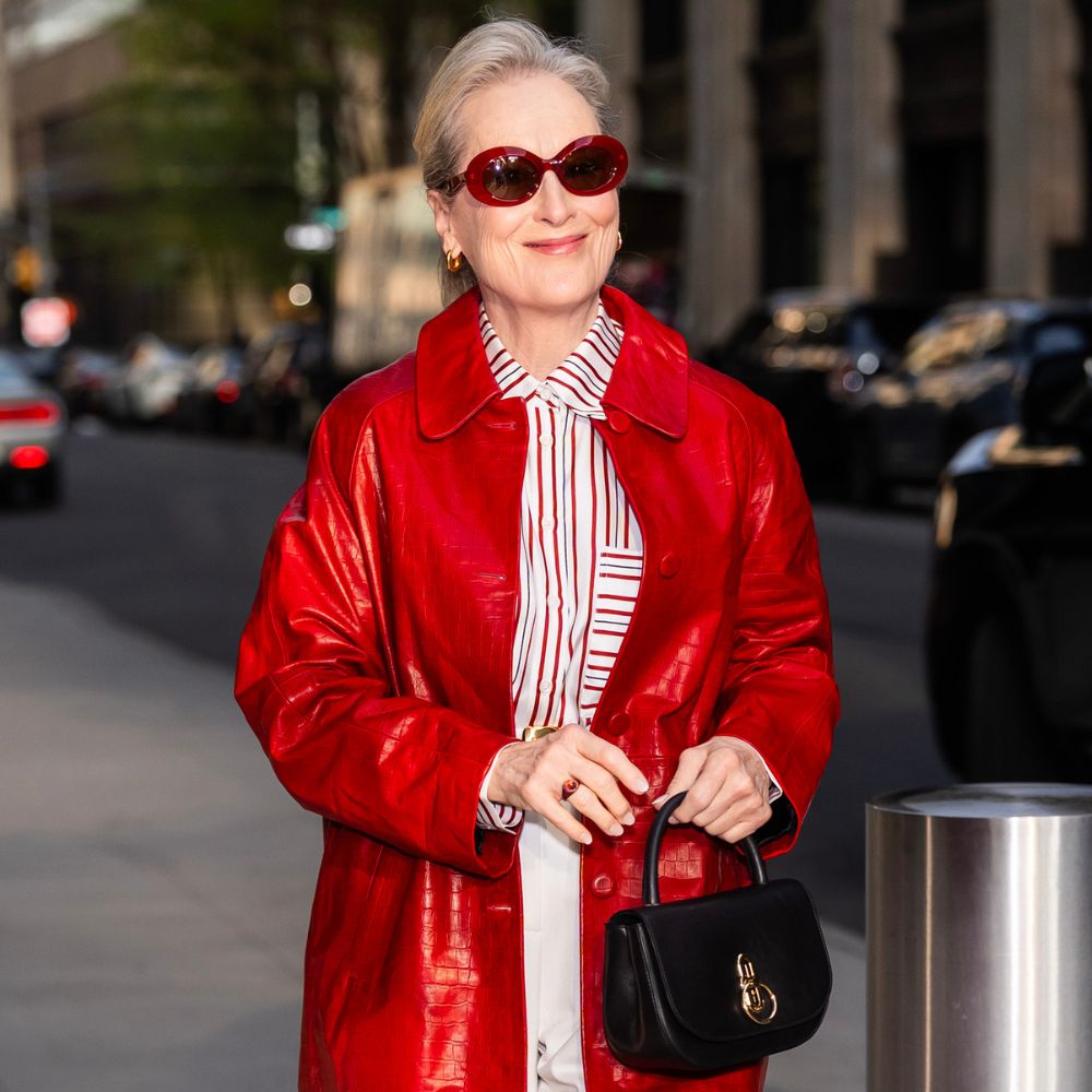 Meryl Streep steps outside in New York wearing a red leather coat with white jeans and red pointed-toe shoes and red sunglasses.
