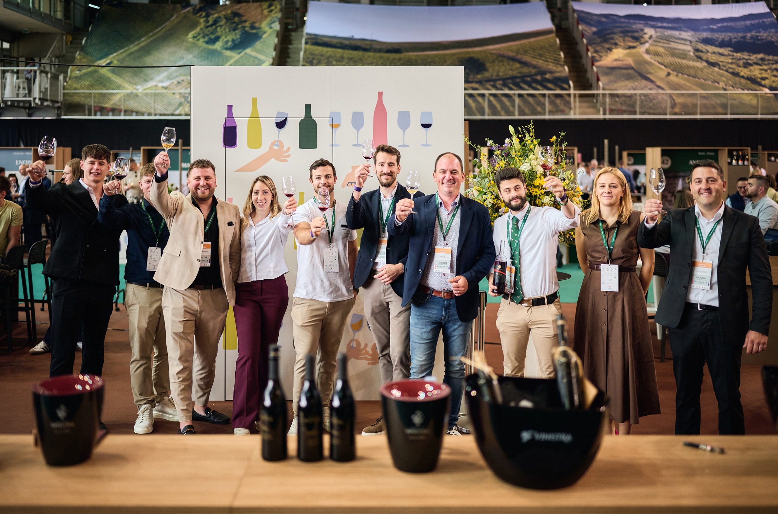 Ten people in their twenties and thirties standing in a row, holding up glasses of wine