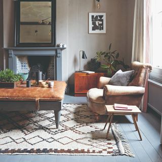 A living room with grey-painted floor boards partly covered in a rug and a matching fireplace at the back of the room