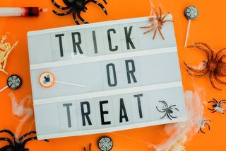 A lightbox with the message Trick or Treat, on an orange background with spider and cobweb decorations.