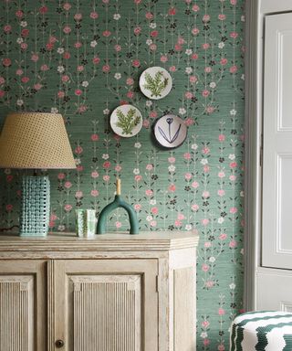 pretty green and pink floral wallpaper with wall plates and wood sideboard with table light