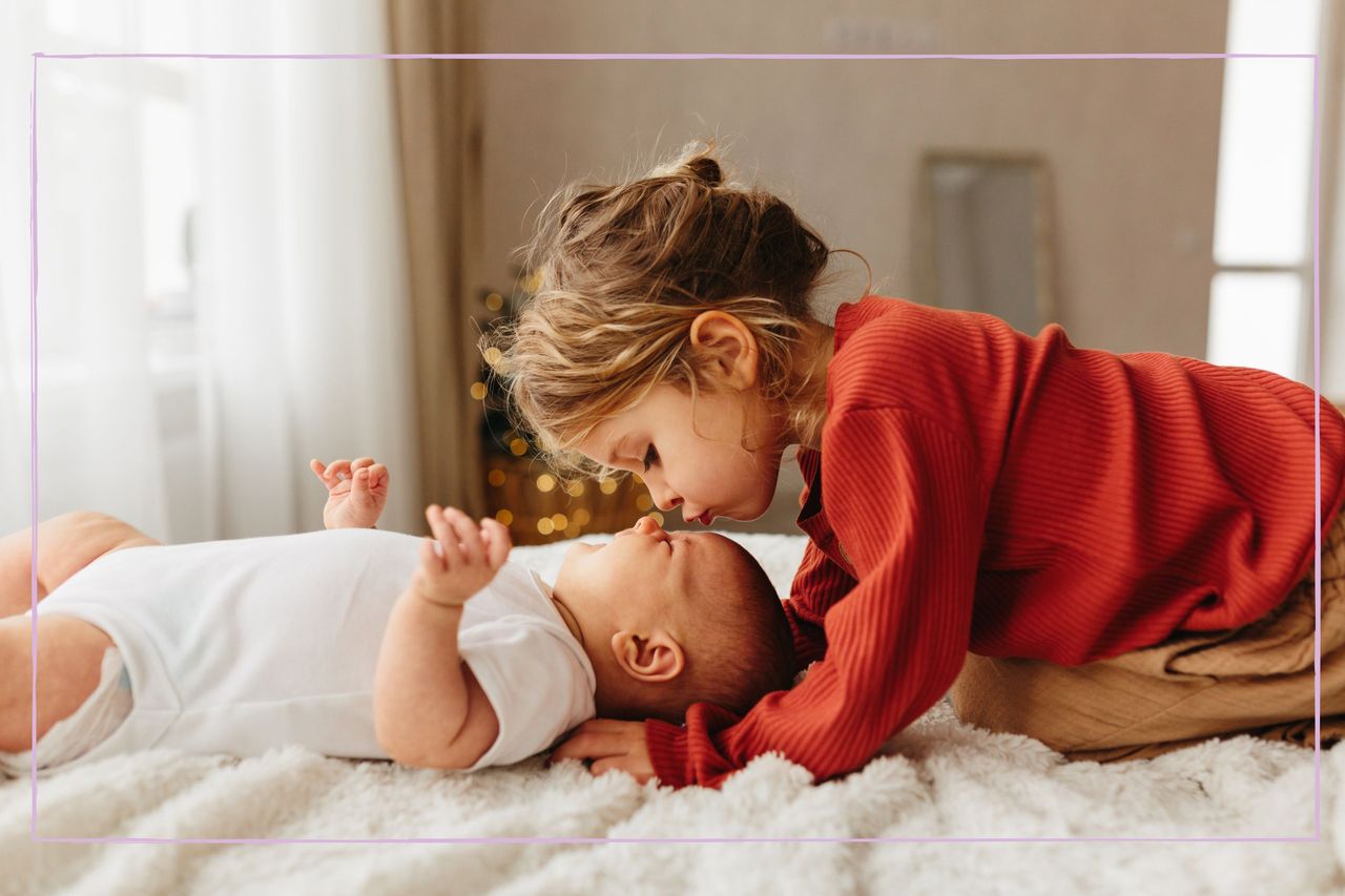 A toddler kissing a baby on the forehead