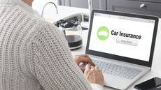 A woman looks at a car insurance shopping website on her laptop at her kitchen island.