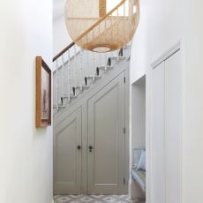 A white hallway with a grey staircase at the end and a rattan pendant lampshade