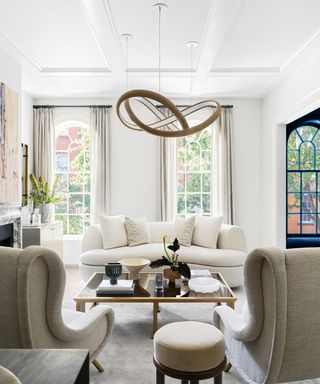 living room with white walls and white sofas and beige armchairs with tall windows
